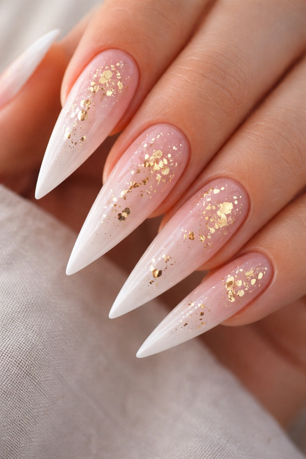 Close-up of soft pink ombre stiletto nails with gold foil accents