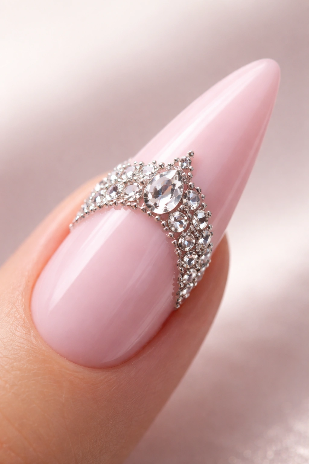Close-up of soft pink curved stiletto nail with rhinestone crown