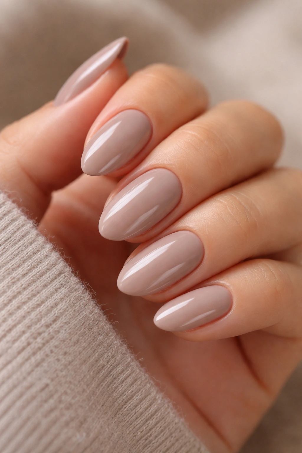 Close-up of soft taupe almond nails on a natural backdrop with a glossy finish