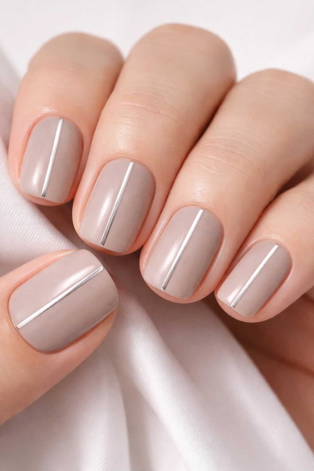Close-up of soft taupe nails with a single silver stripe on short squoval nails