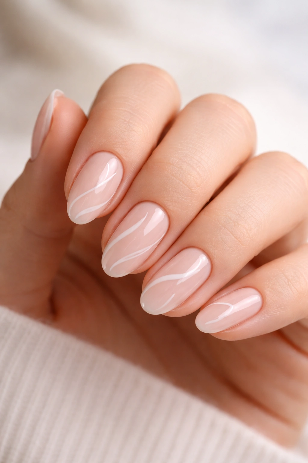 Close-up of short almond nails with thin white swirl patterns on a nude base