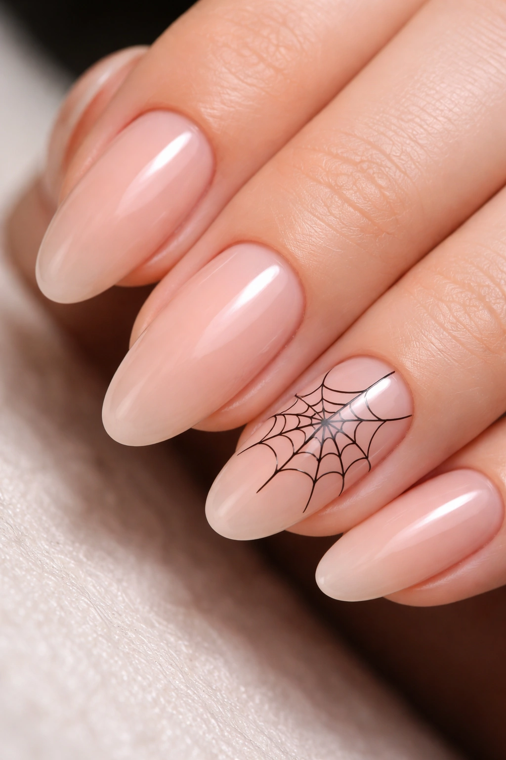 Close-up of nude nails with delicate black spiderweb design