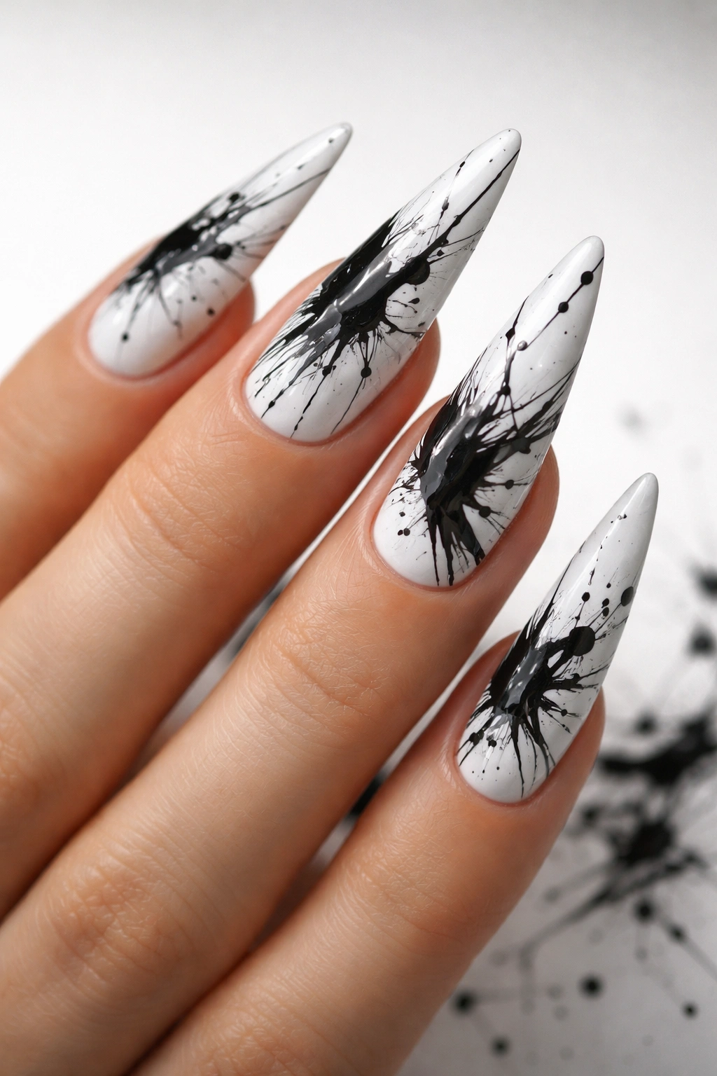 Close-up of stiletto nails with black splatter abstract art on white base