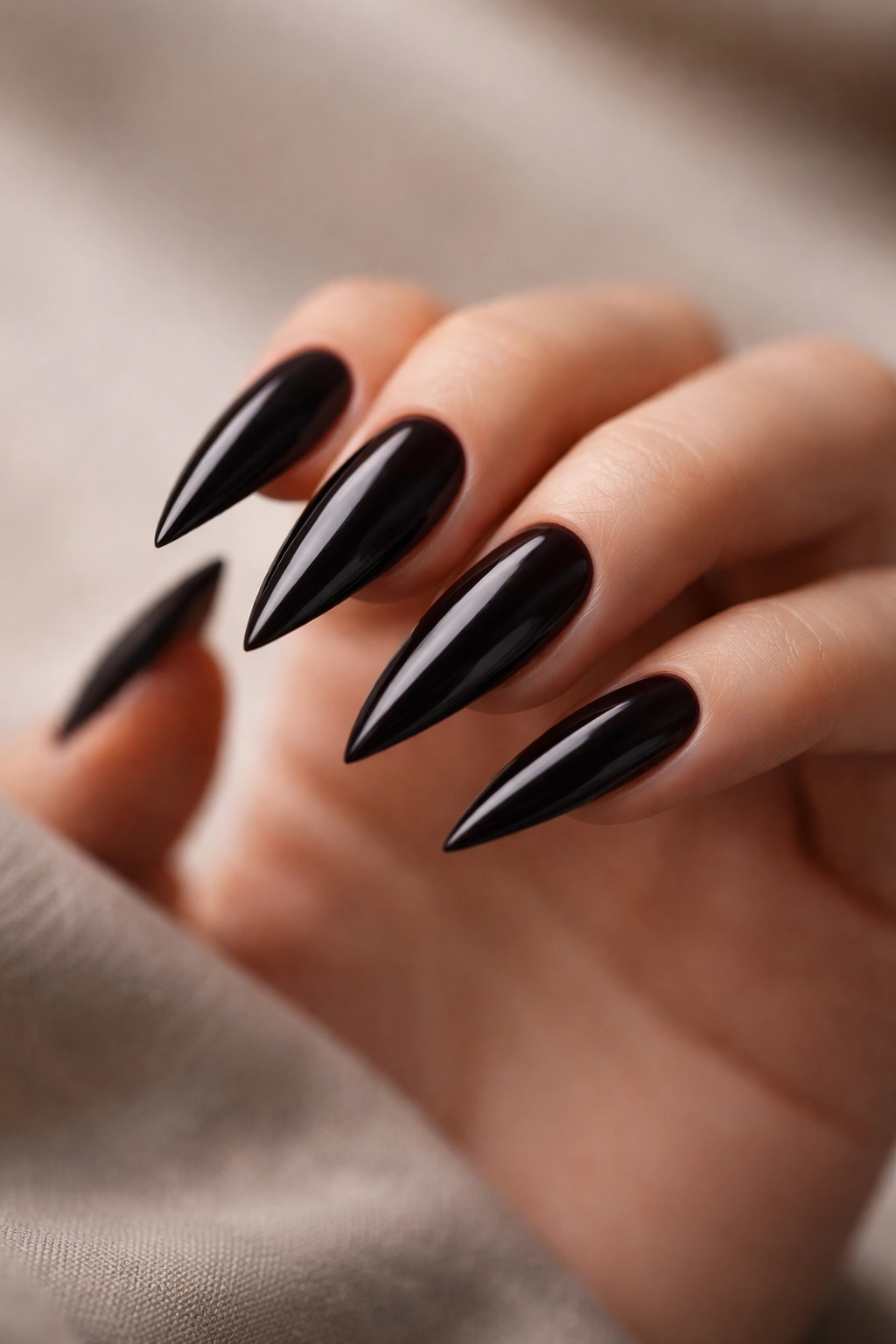 Close-up of glossy black stiletto nails with sharp points on a hand against a neutral background