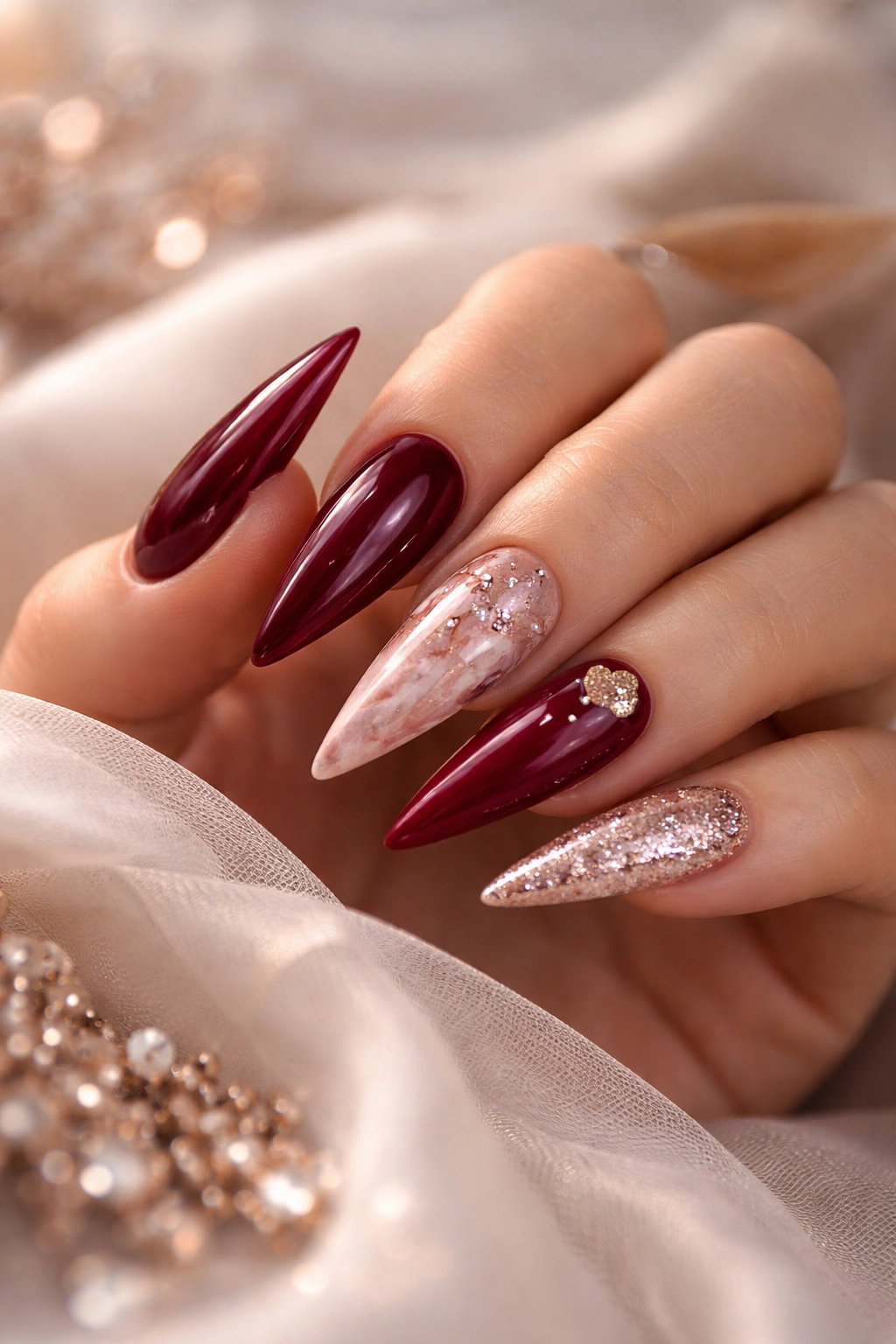 Close-up of a hand with romantic stiletto nails in red, burgundy, nude rose-gold, ombre and marble designs