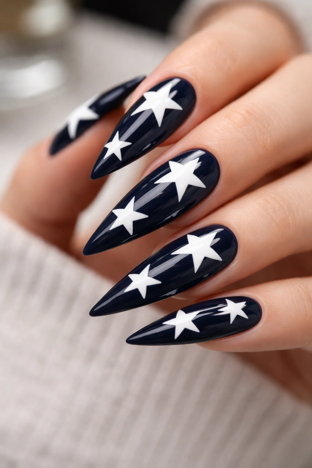 Close-up of white five-point stars on a dark navy stiletto nail