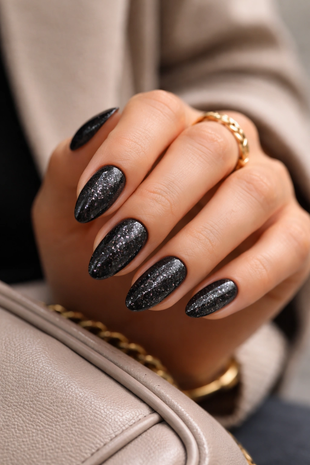 Close-up of short almond nails with black glitter, shown on a neutral background.