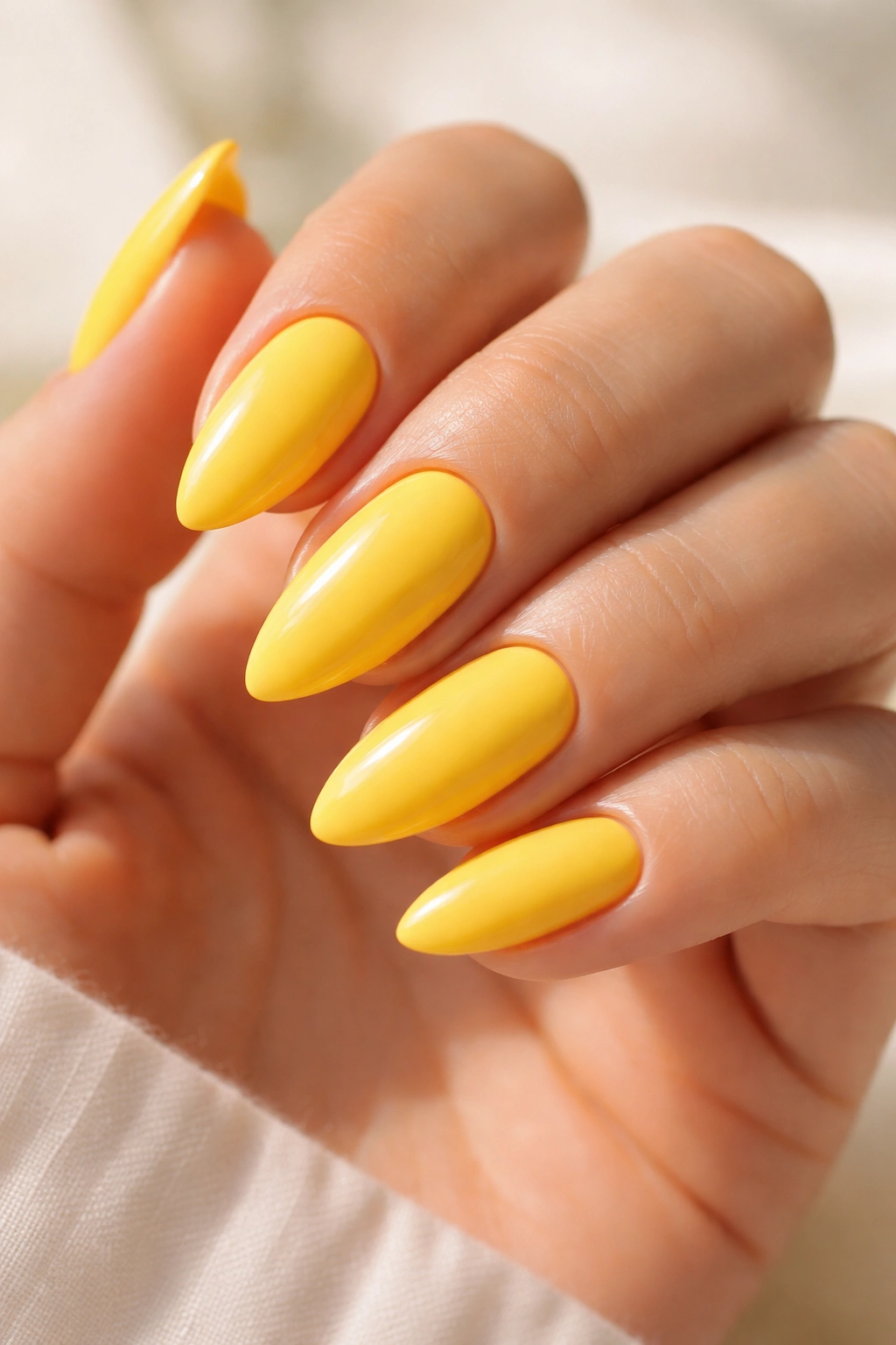 Close-up of sunny yellow almond nails with opaque two-coat gloss on a hand