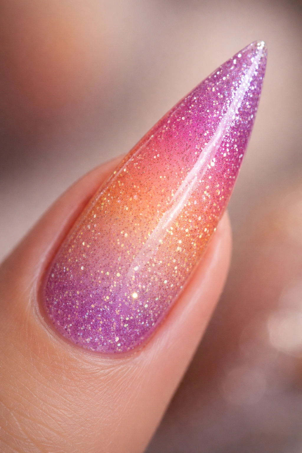 Close-up of a stiletto nail with peach-pink-purple gradient and rose gold glitter ombre on a neutral background