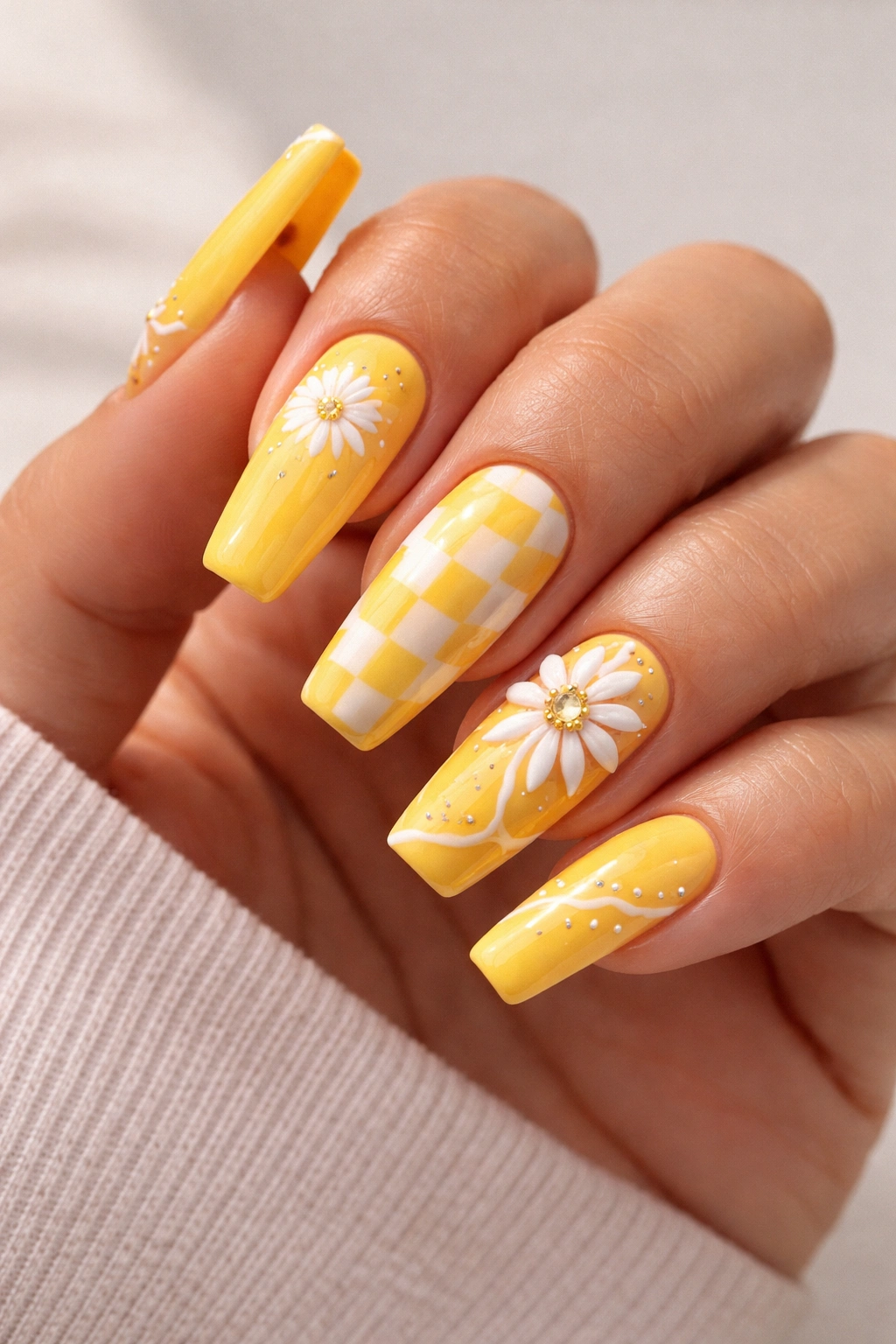 Close-up of sunshine yellow coffin nails with nail art on a hand against a plain backdrop