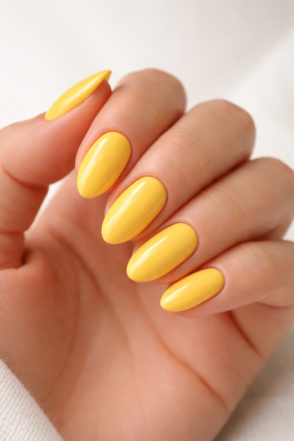 Close-up of short almond nails painted bright sunshine yellow with a glossy finish