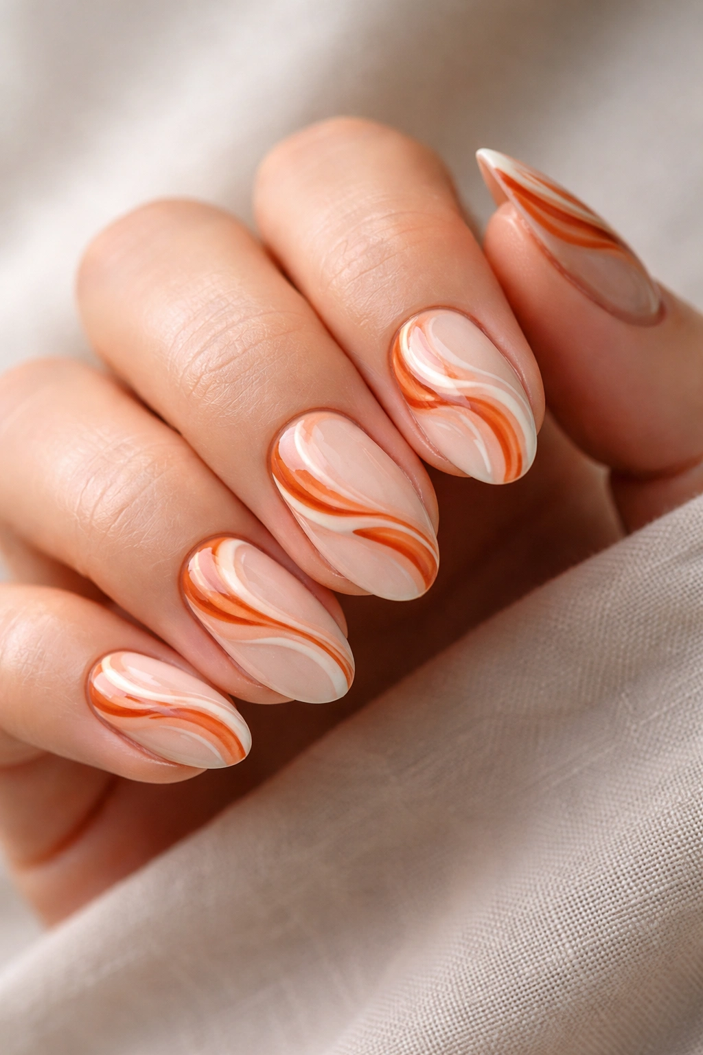 Short almond nails with burnt orange and cream swirls on a soft base.