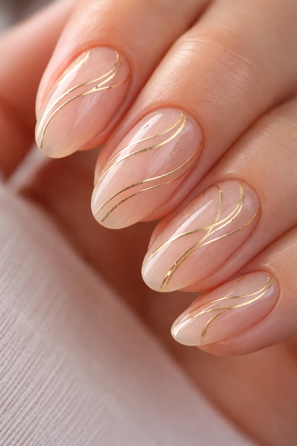 Close-up of short almond nails with sheer base and delicate gold swirls