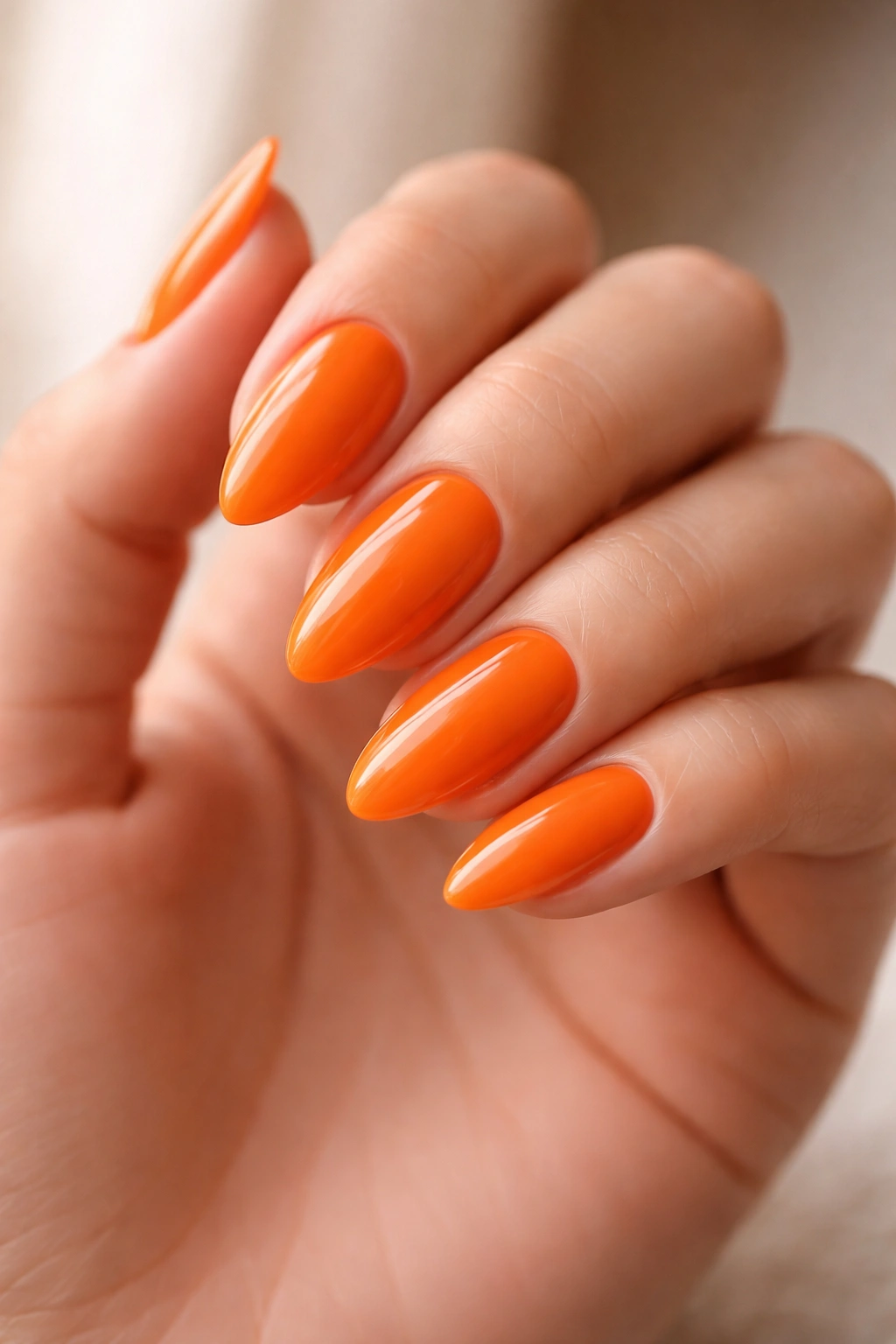 Close-up of tangerine almond nails with glossy orange polish