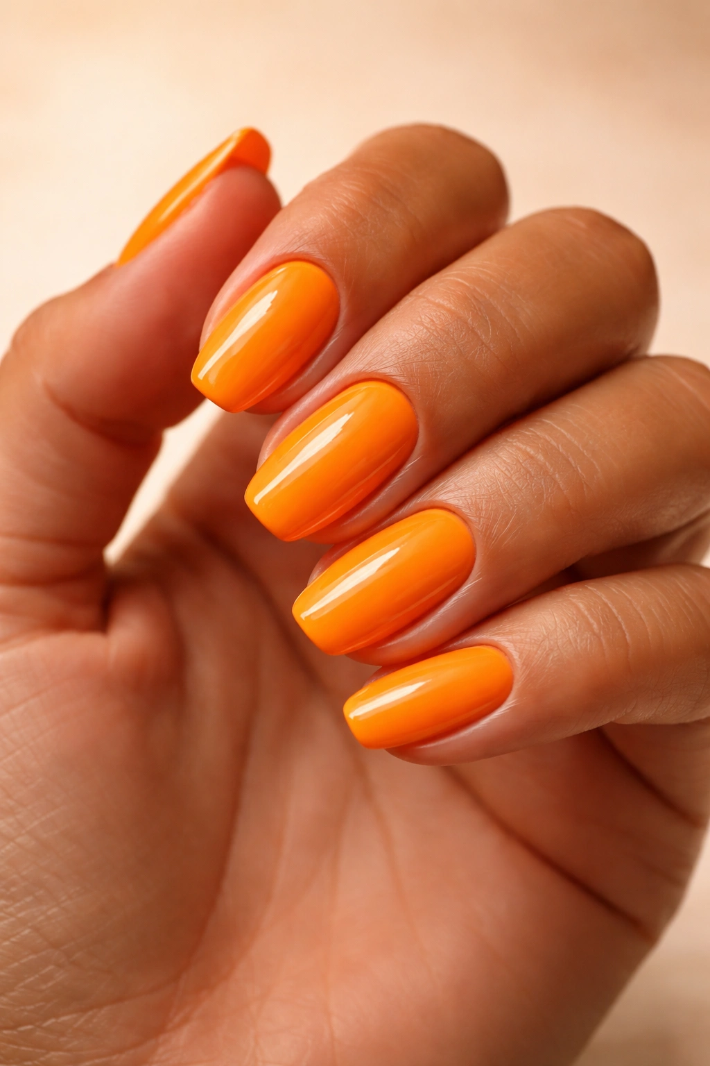 Close-up of a tanned hand with bright tangerine nails.