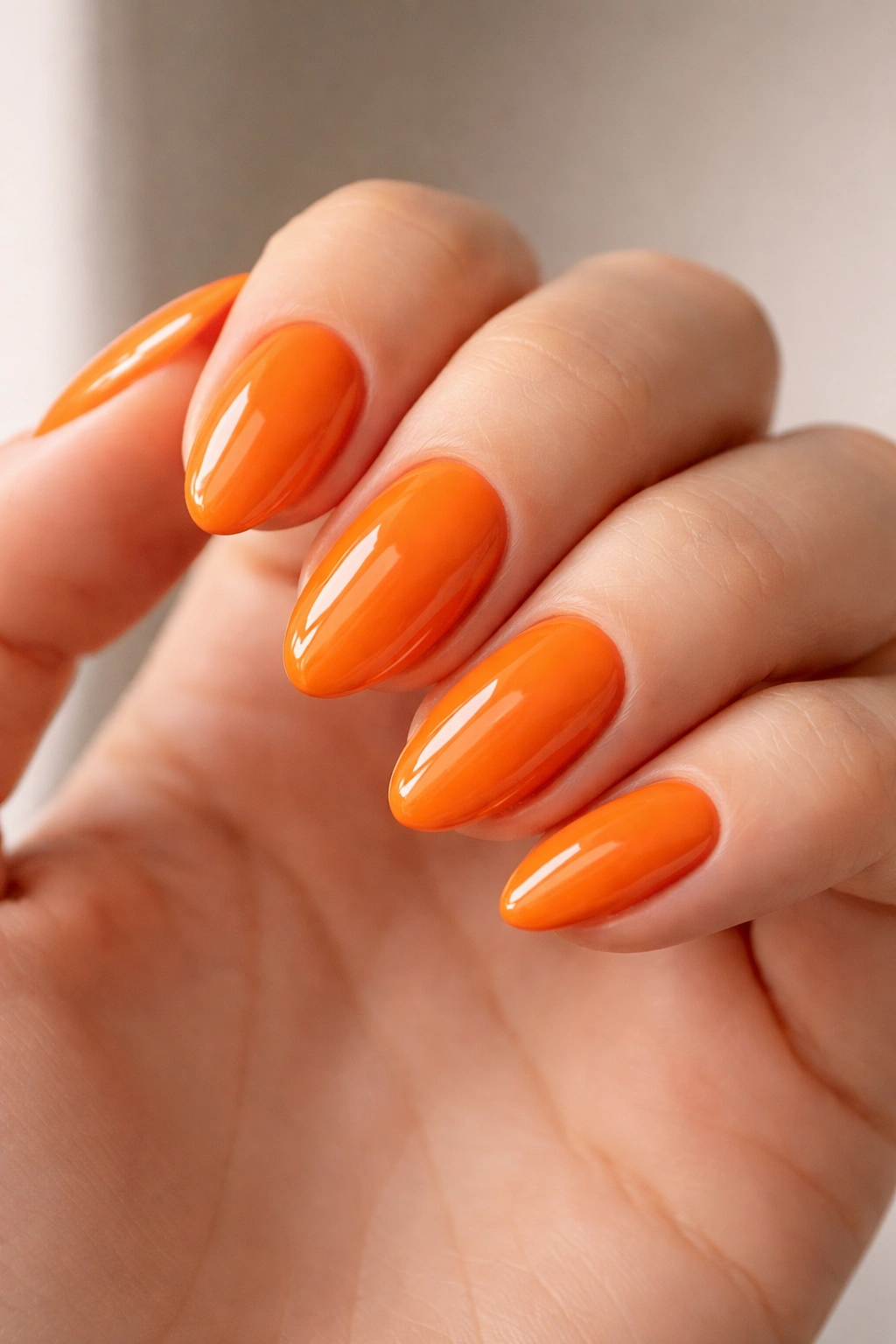 Close-up of tangerine orange nails on a short almond shape with a high shine