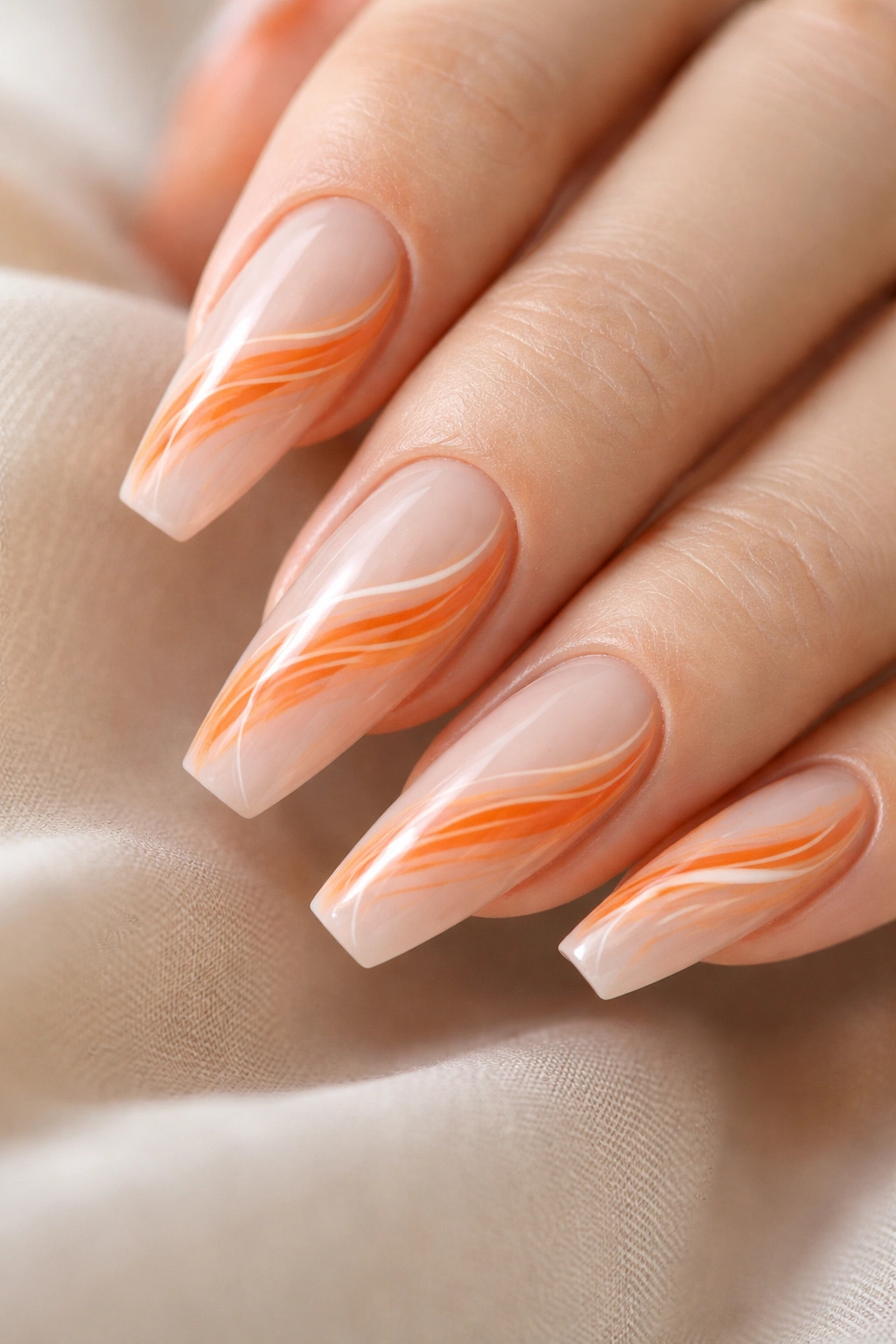 Close-up of tangerine swirl nails on sheer base with glossy finish