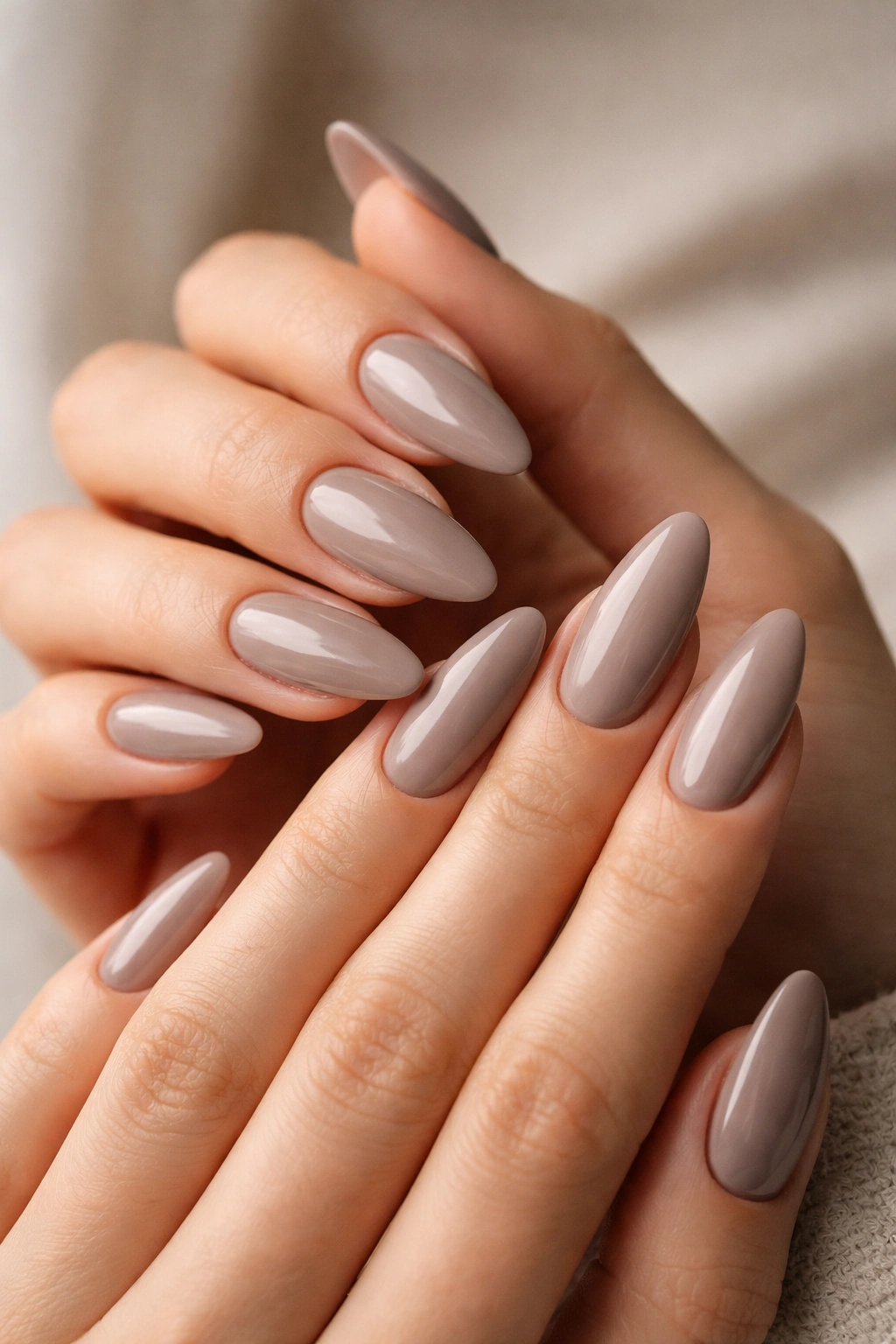 Taupe almond nails with glossy finish on a neutral backdrop
