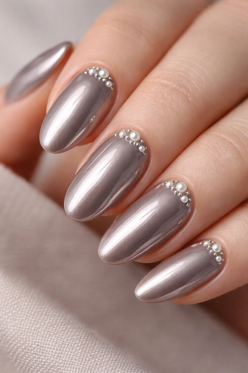 Close-up of taupe chrome nails with pearl accents near the cuticle.