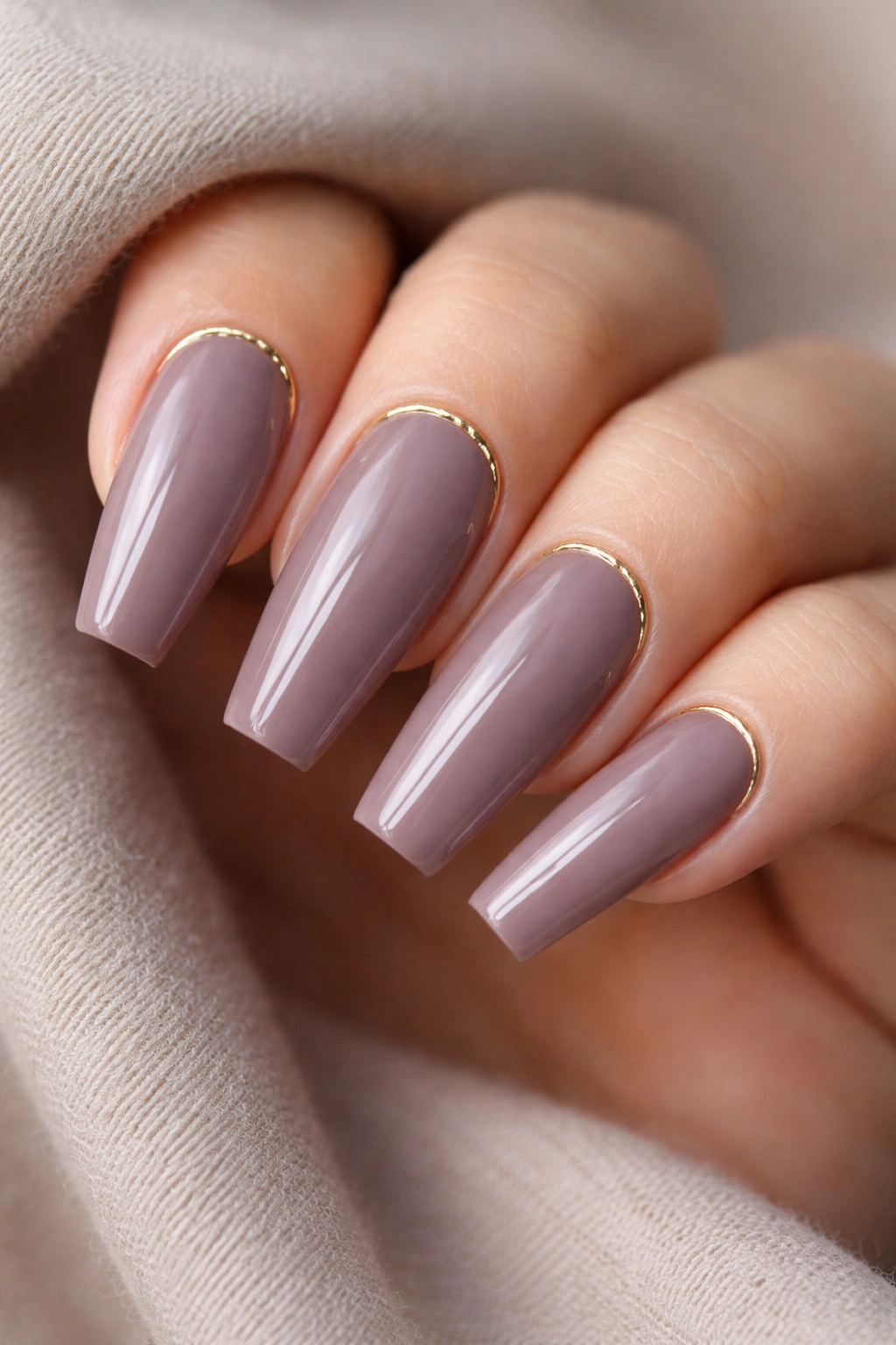 Close-up of taupe-mauve nails with a fine gold arc at the cuticle