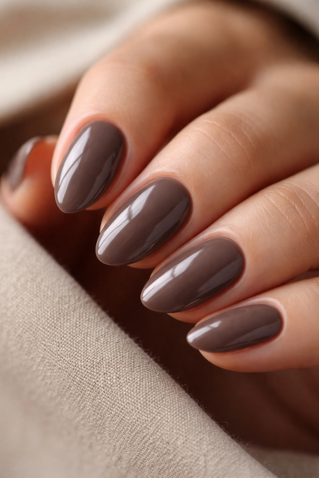 Close-up of a short almond nail in dark taupe with a glossy finish