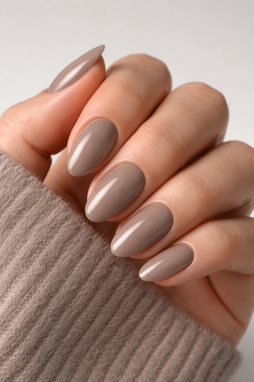 Close-up of taupe almond press-on nails on a hand with a neutral background