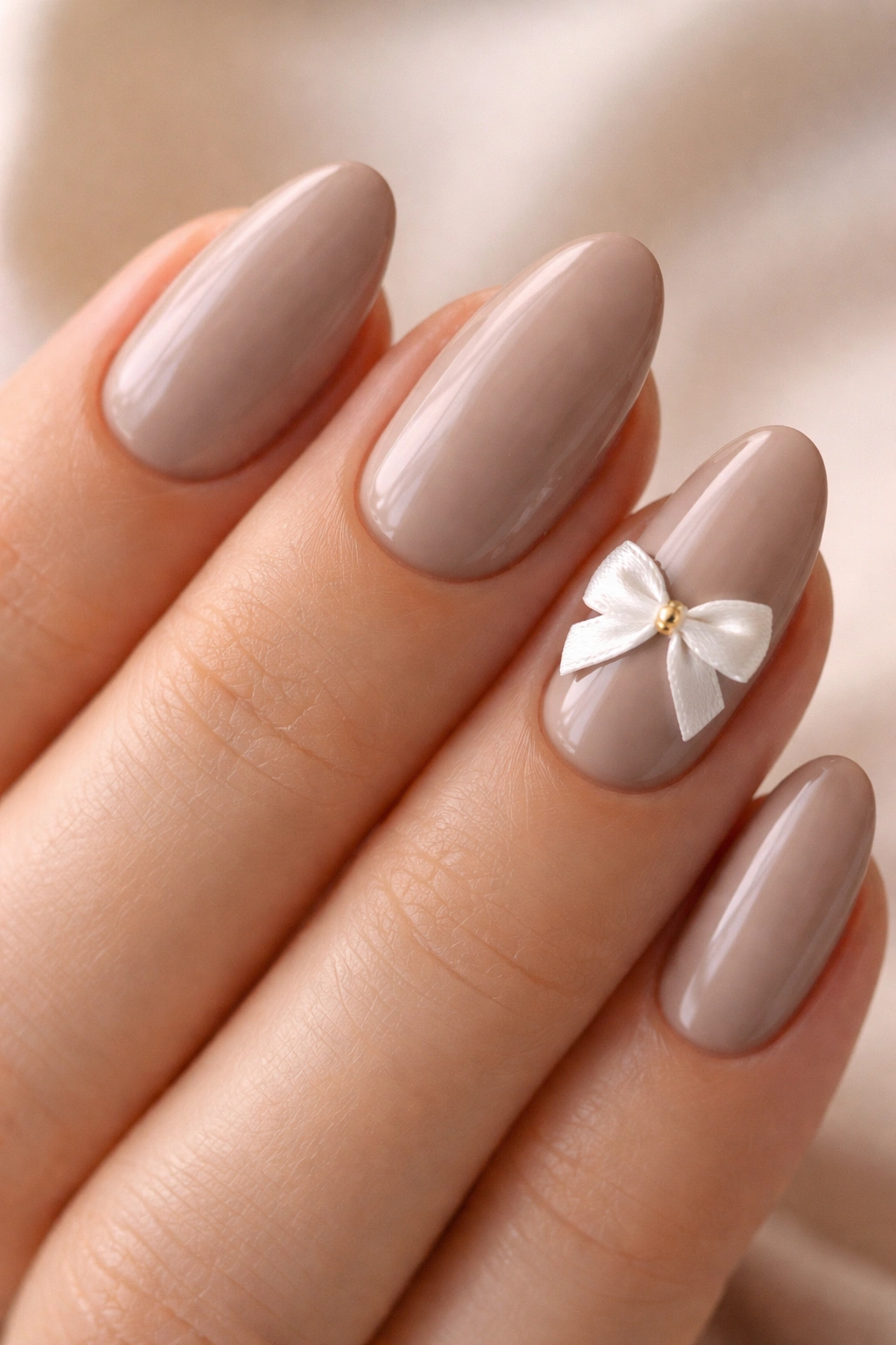 Close-up of creamy taupe almond nails with a satin white bow