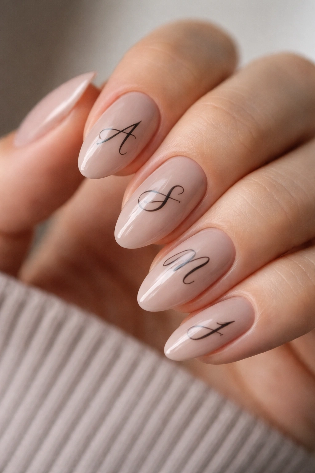 Close-up of short almond nails in soft taupe with black calligraphy strokes