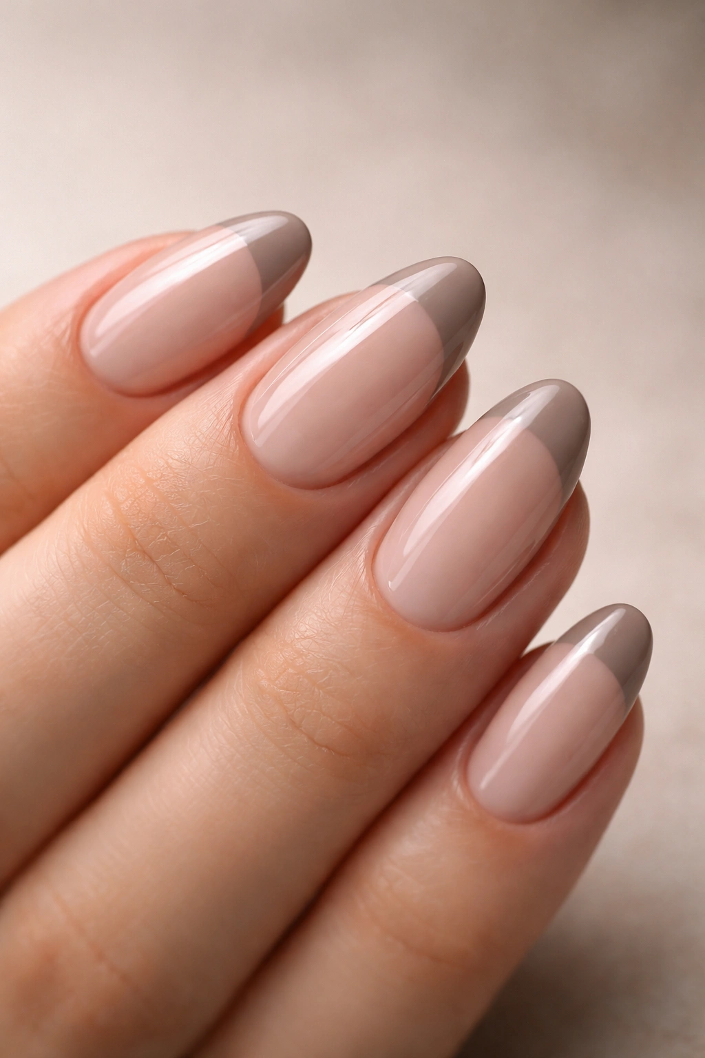 Close-up of short almond nails with taupe French tips and glossy finish