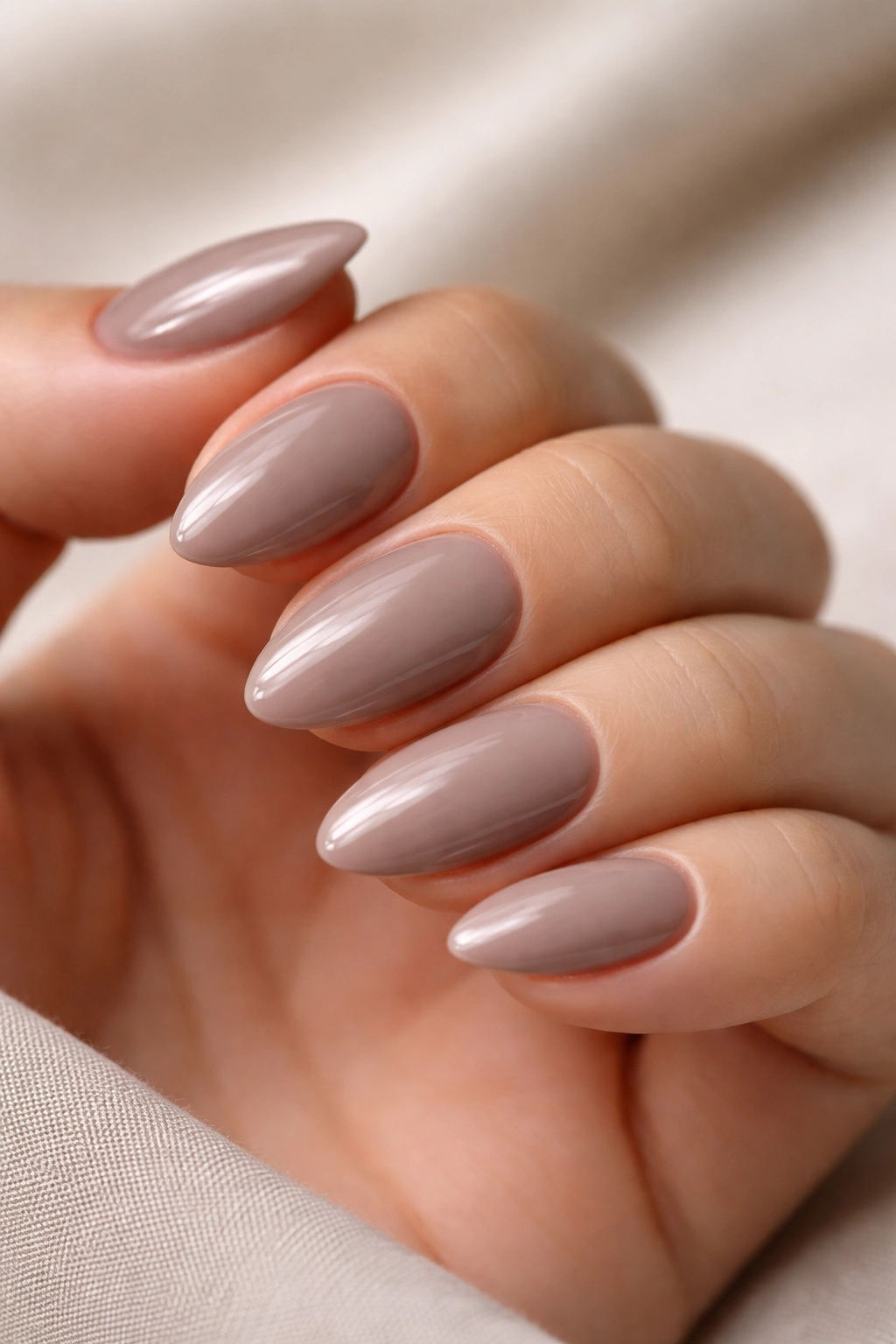 Close-up of short almond nails in glossy taupe on a neutral hand
