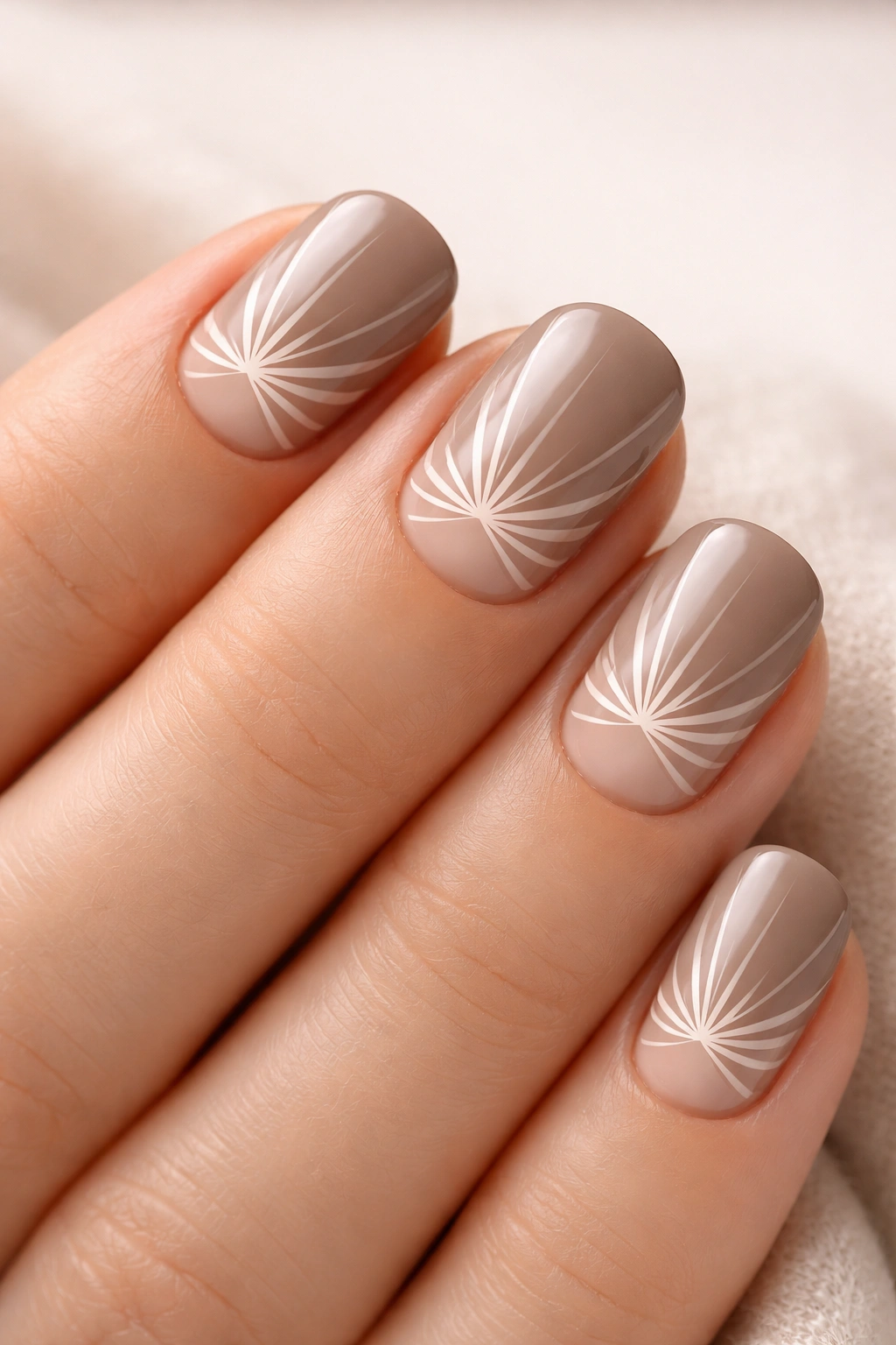 Taupe nails with white sunburst negative-space design on short squoval nails, studio lighting.