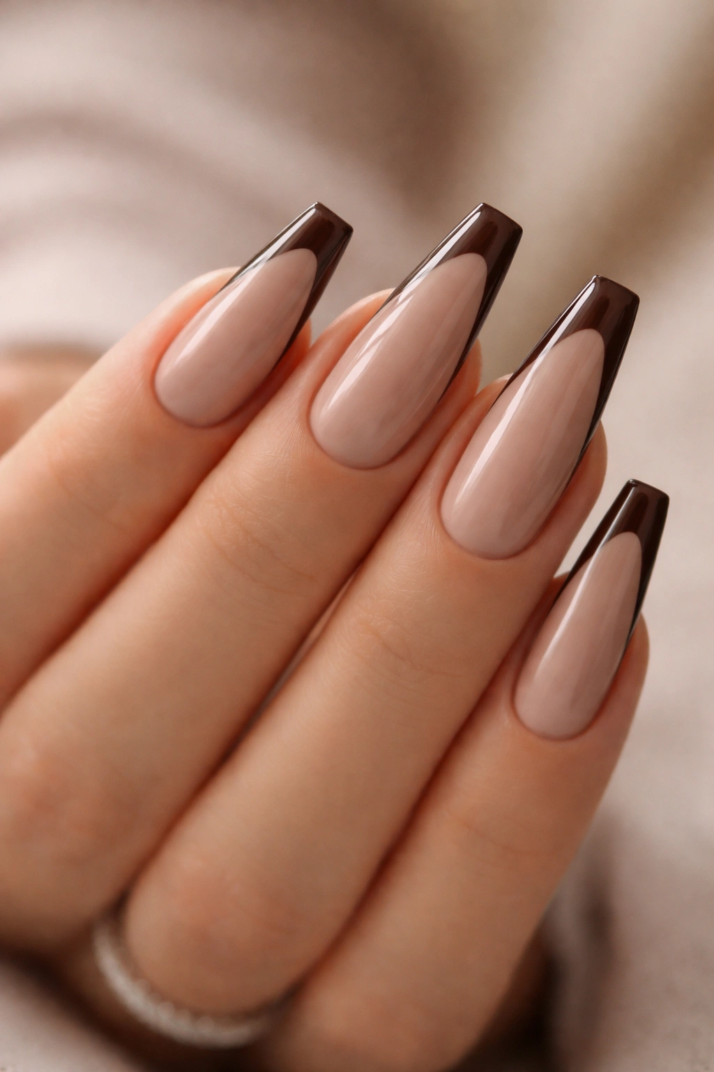 Close-up of taupe nude ballerina nails with espresso side tips on a hand