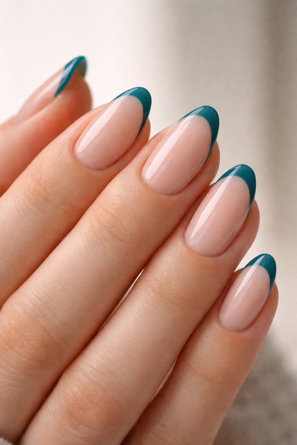 Close-up of teal French tips on a nude base on short almond nails