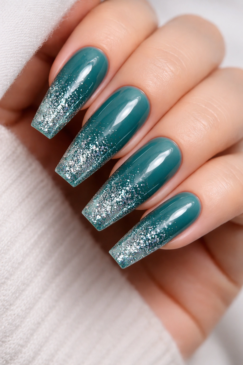 Teal coffin nails with gradient glitter fade on a bare hand.