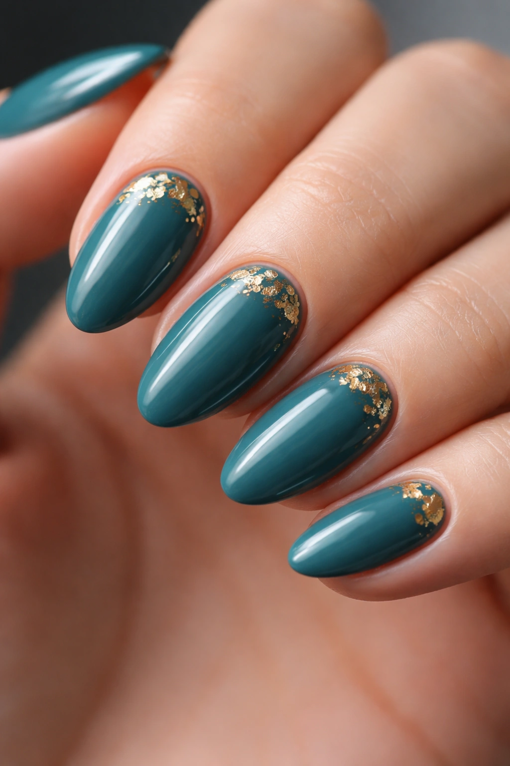 Close-up of teal nails with thin gold foil accents on short almond shape