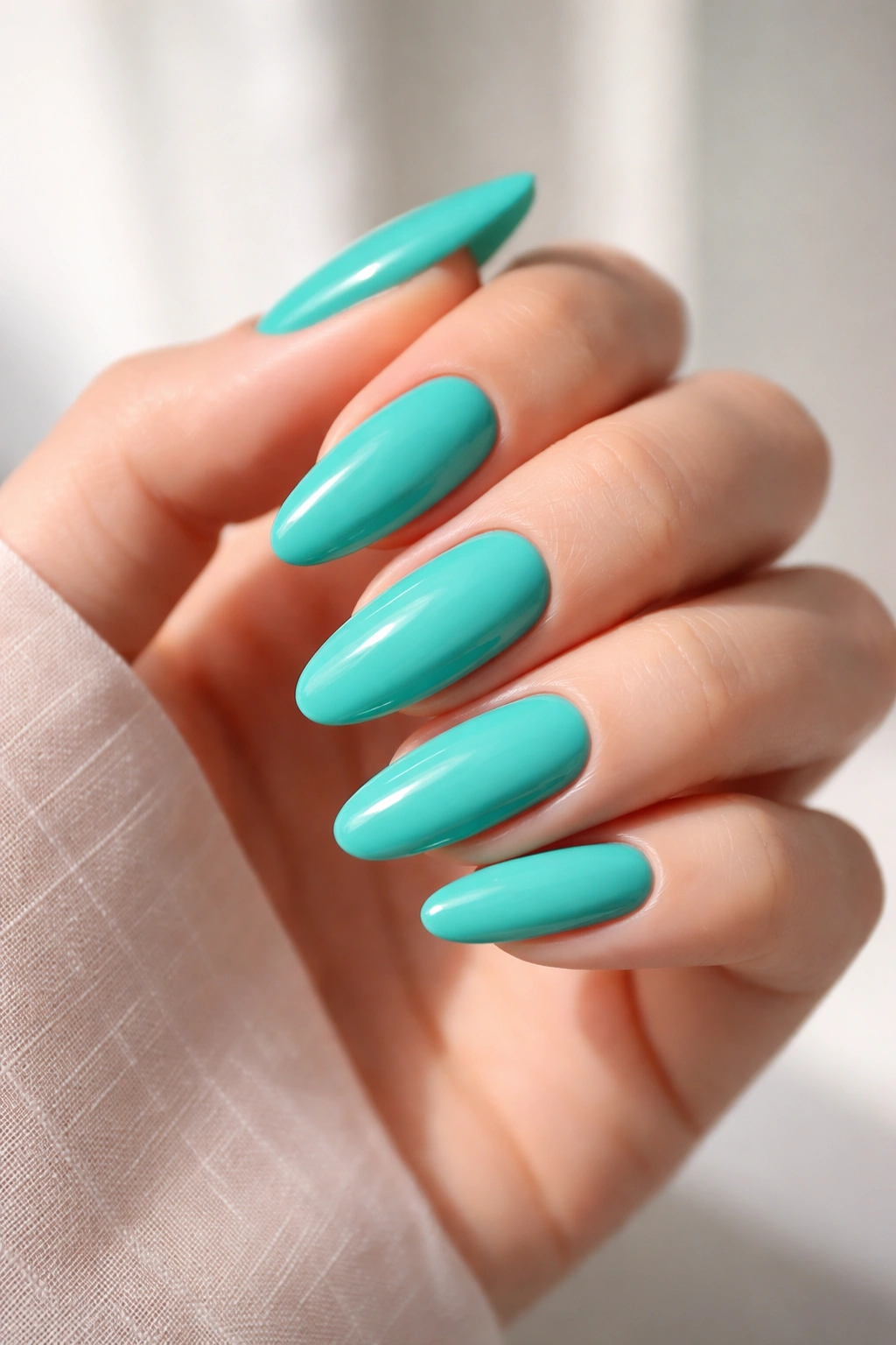 Close-up of long oval nails in bright teal with glossy finish