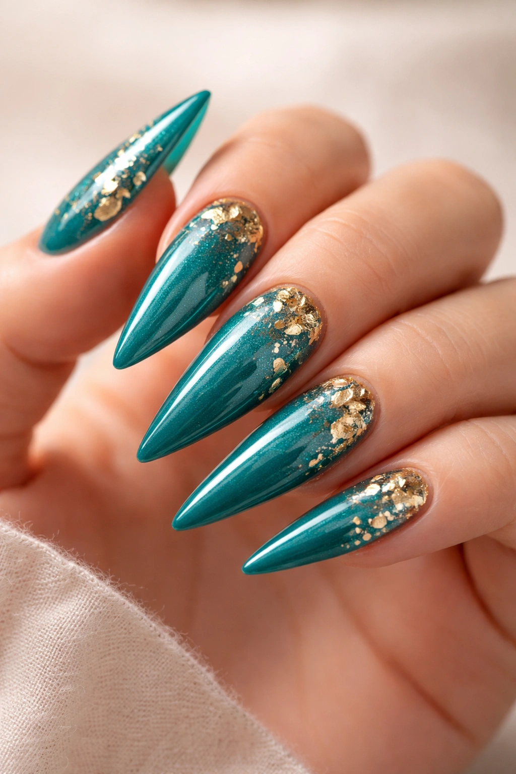 Teal stiletto nails with gold leaf accents close-up