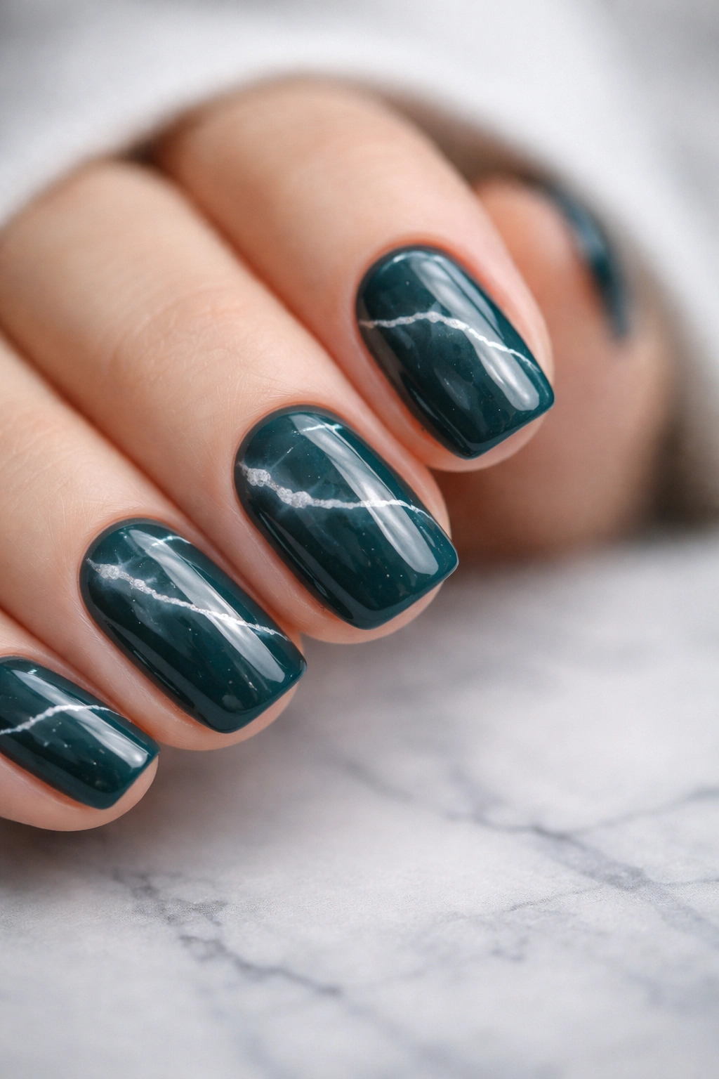 Deep teal nails with white marble veining on short squoval shape