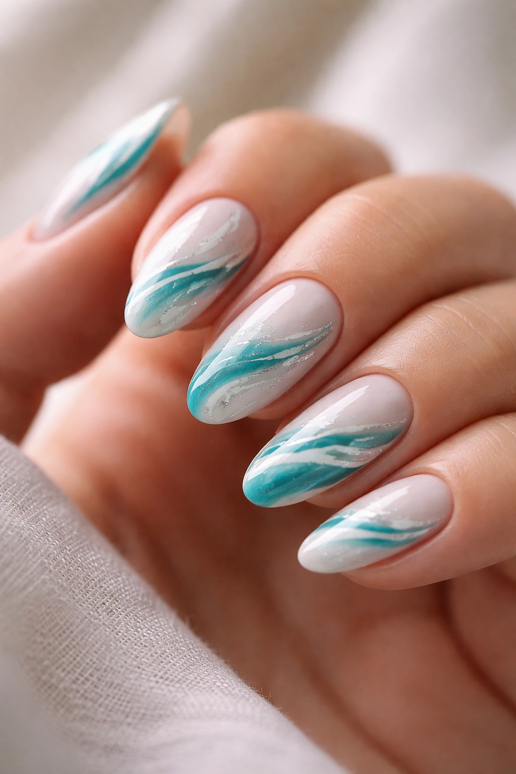 Close-up of short almond nails with teal and white marble swirls on a neutral background