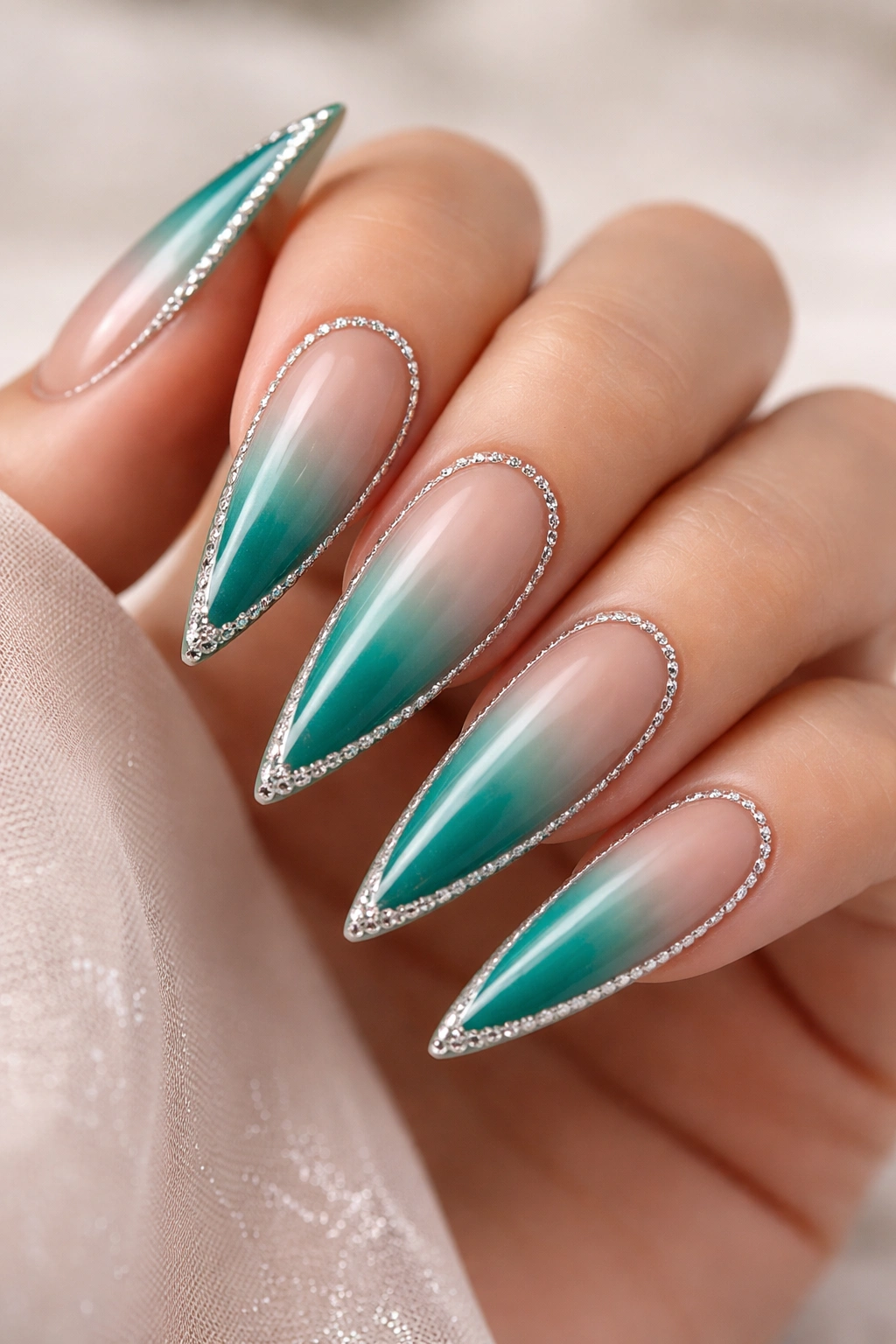 Close-up of teal ombre stiletto nails with a delicate rhinestone frame