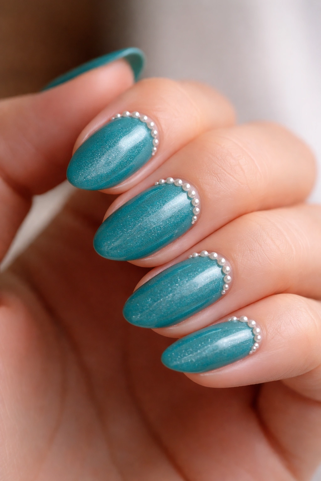 Short almond nails with a row of tiny pearls on teal base
