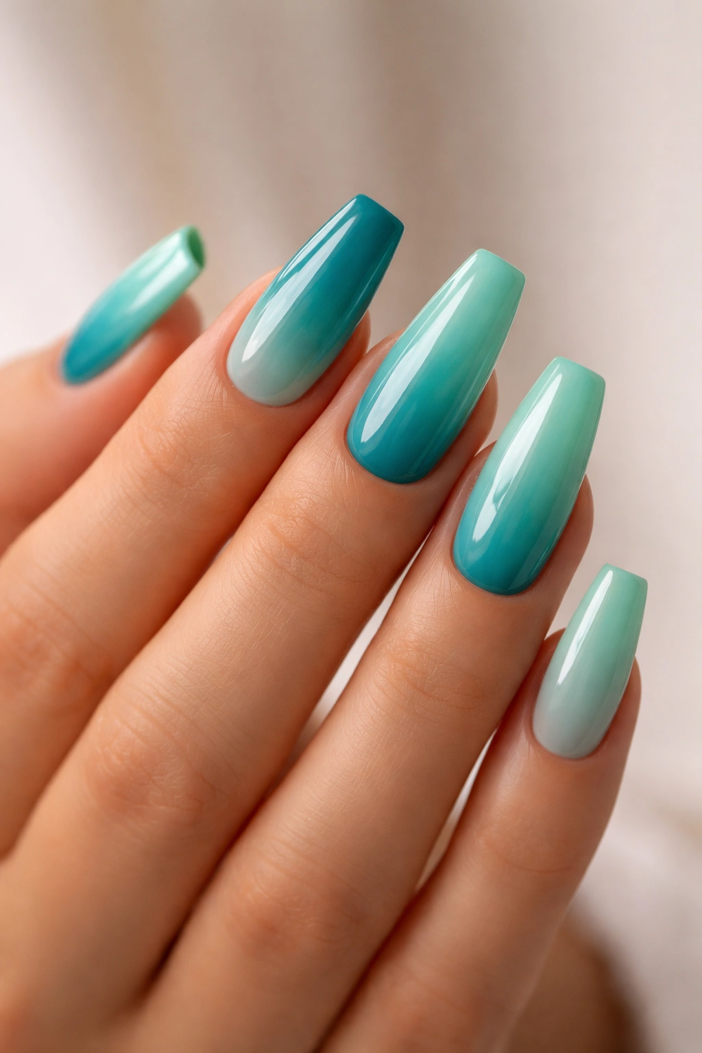 Close-up of teal to seafoam ombre coffin nails on a hand with a glossy finish