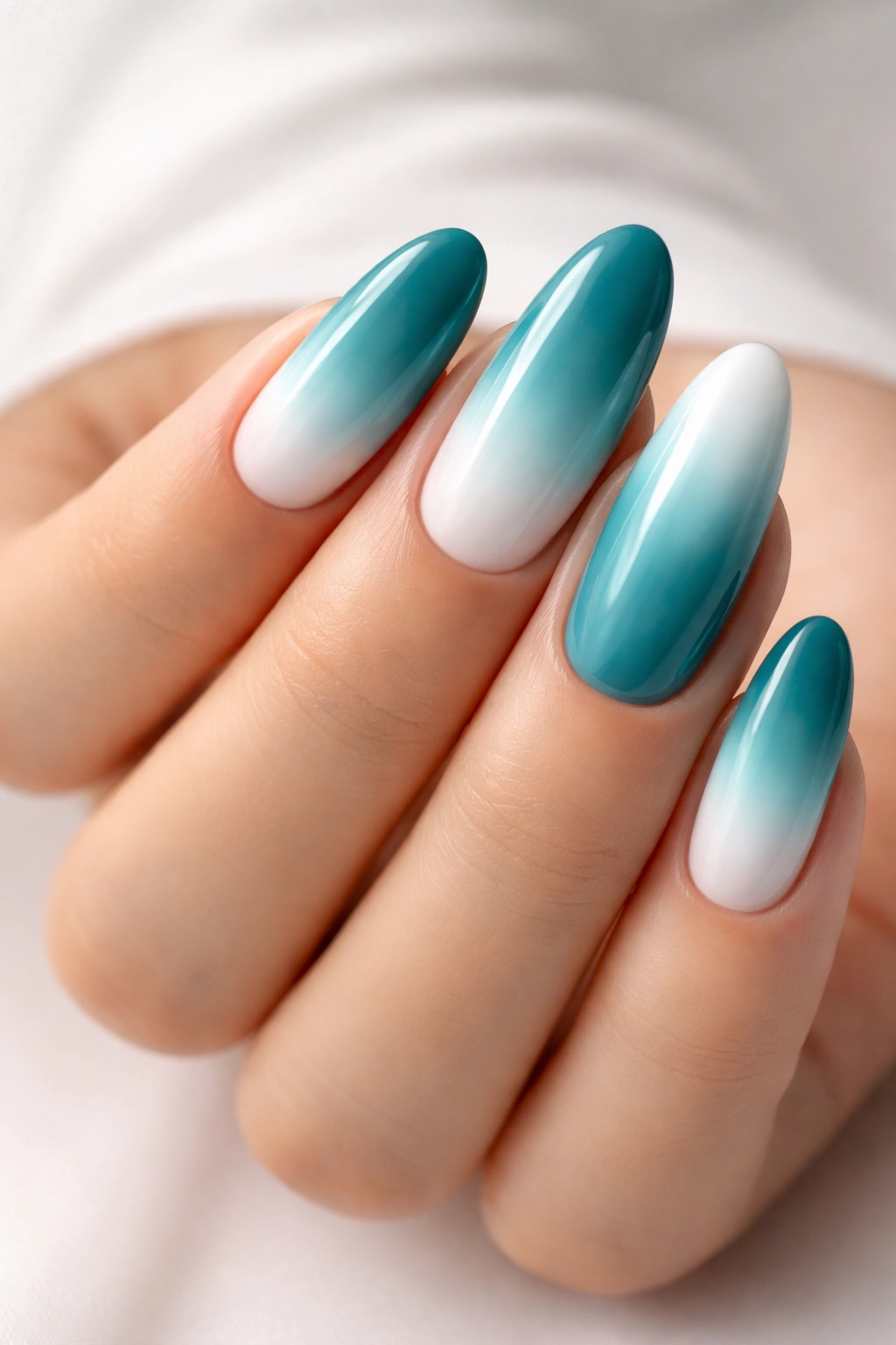 Close-up of long oval nails in teal to white ombre with glossy finish