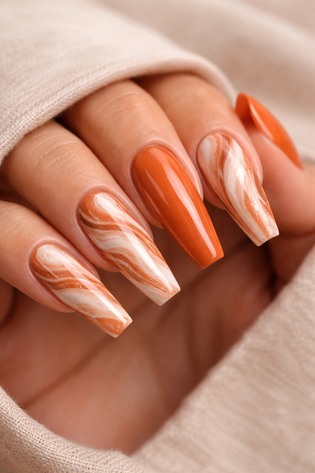 Close-up of ballerina nails with terracotta marble swirls on a soft beige base.