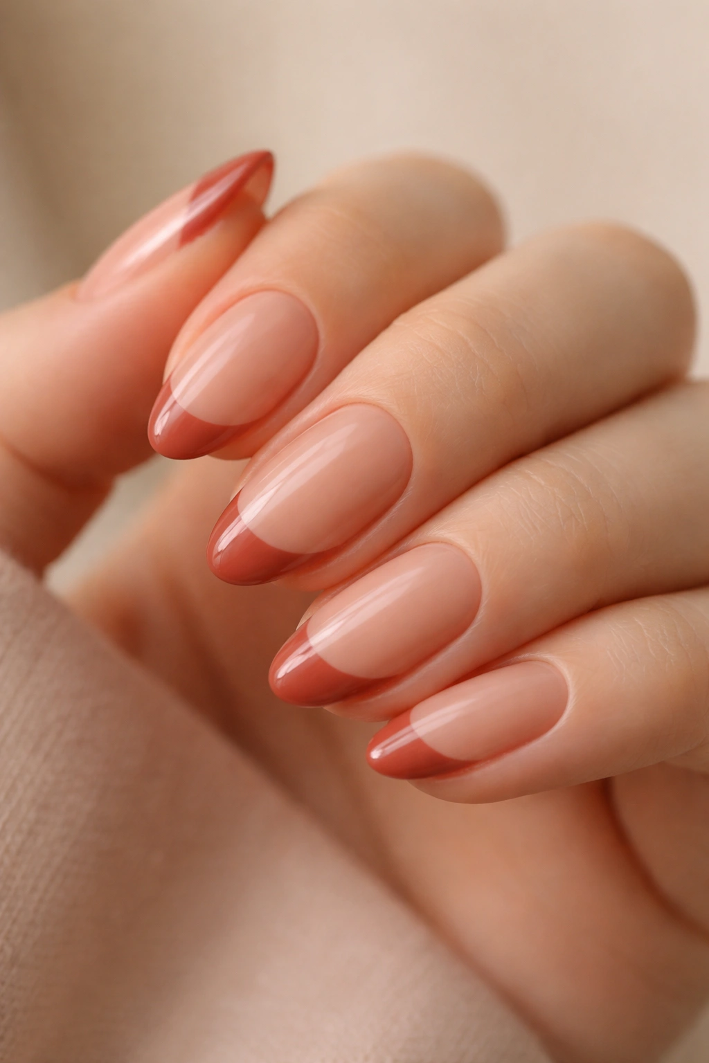 Close-up of a short almond nail with terracotta French tip on a warm nude base