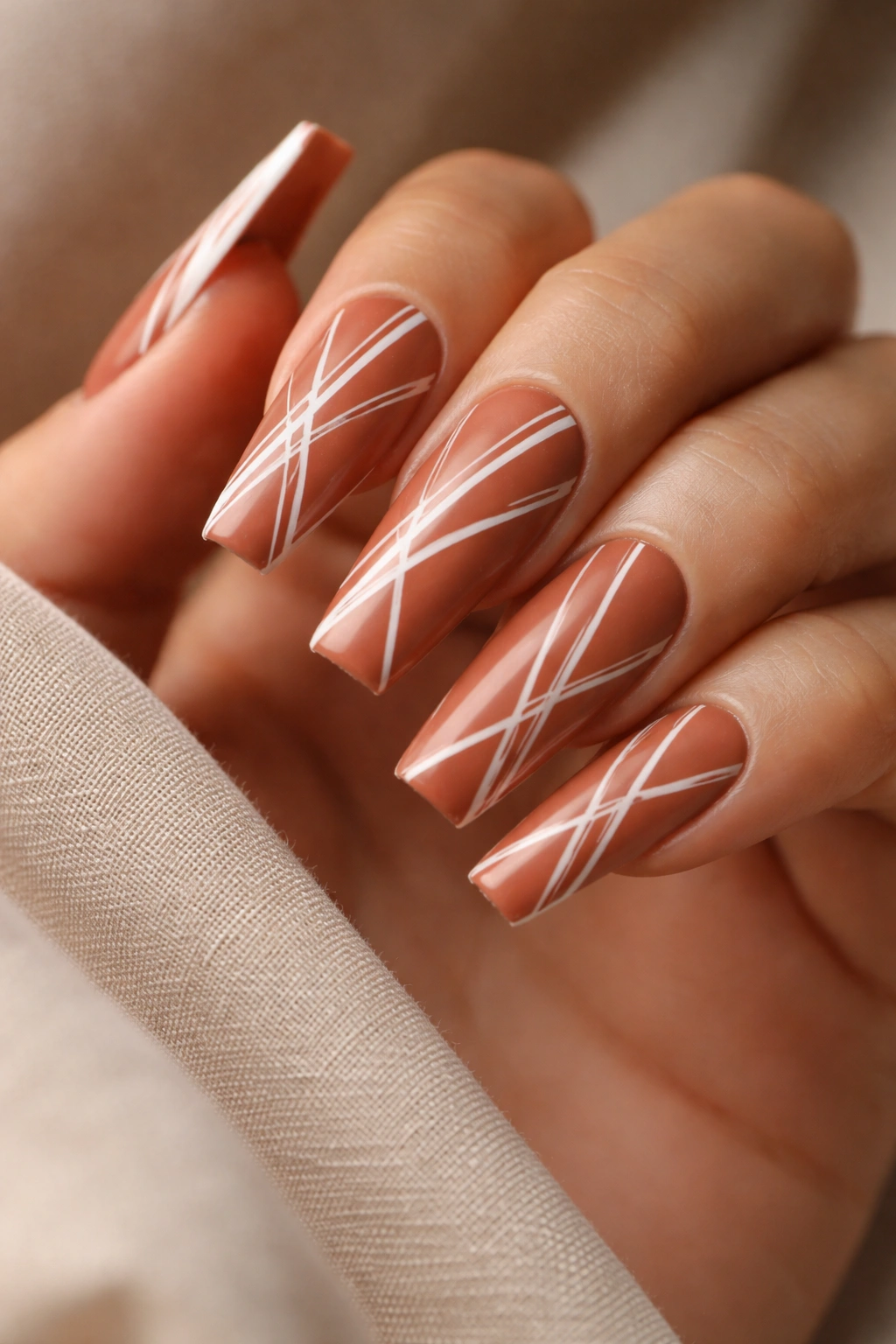 Close-up of coffin nails with warm terracotta polish and white geometric line art.