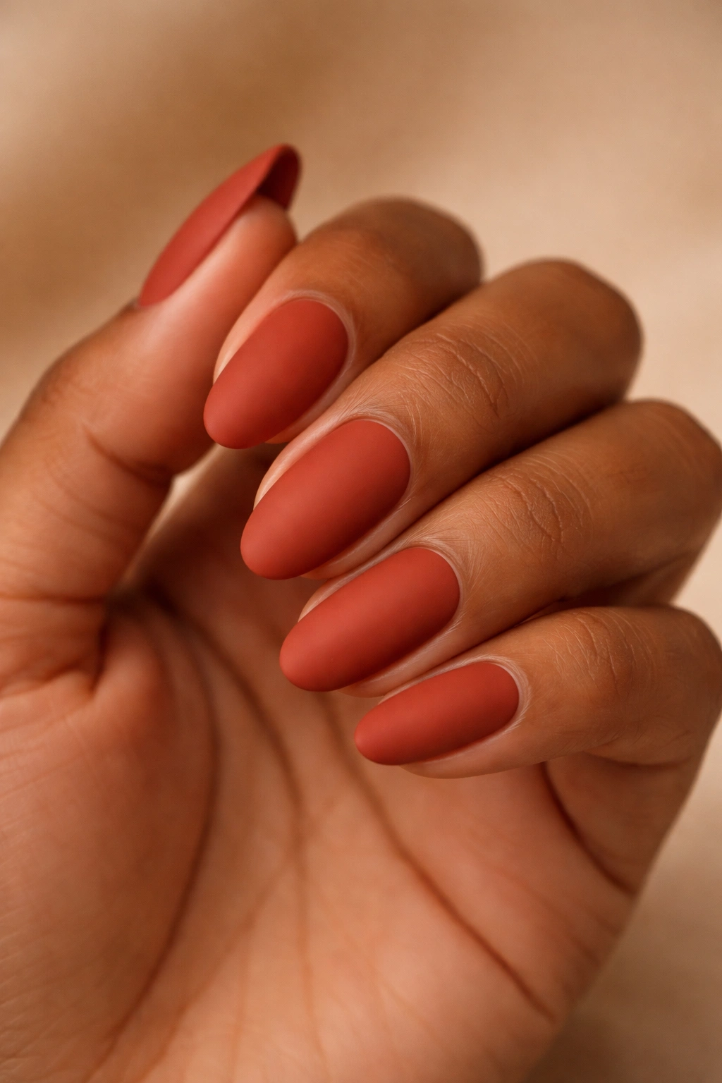 Close-up of nails painted terracotta red with a matte finish on warm brown skin
