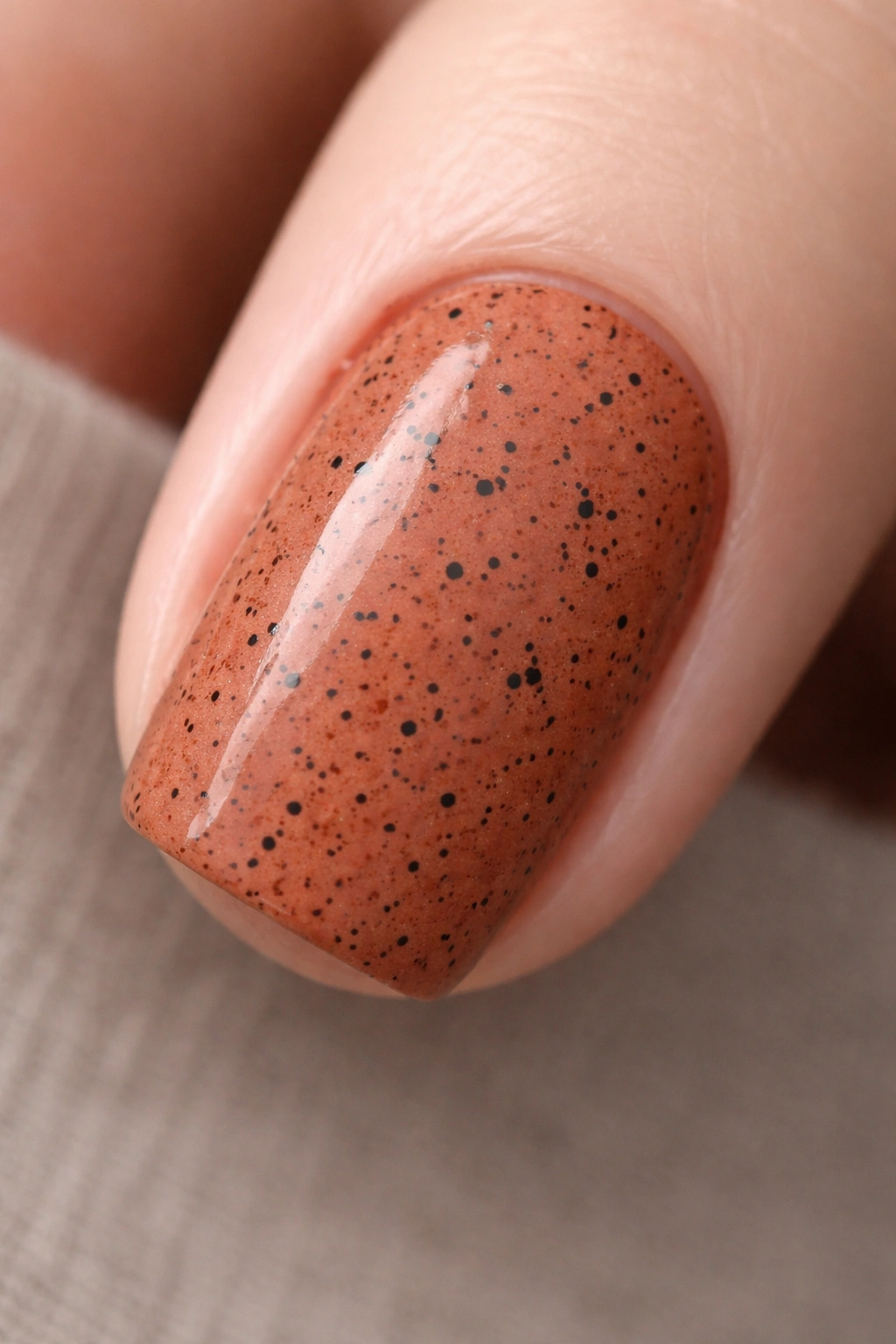 Close-up of terracotta nail with black specks on a neutral background