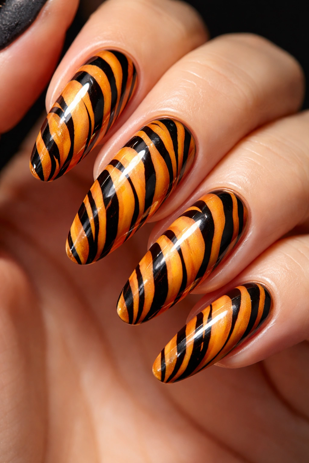 Close-up of tiger print nail design with orange base and black stripes.