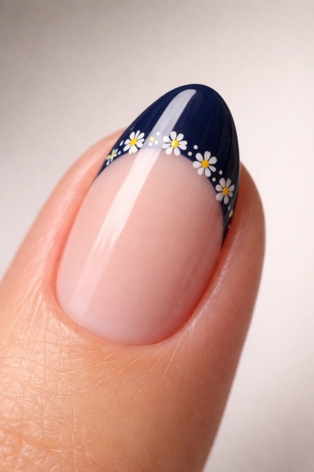 Close-up of a short almond nail with navy tip and micro white floral daisies near the contact line